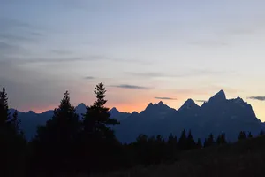 Orange sunset behind silhouette of Grand Tetons 