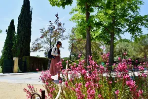 A woman walks between trees and flowers in a park